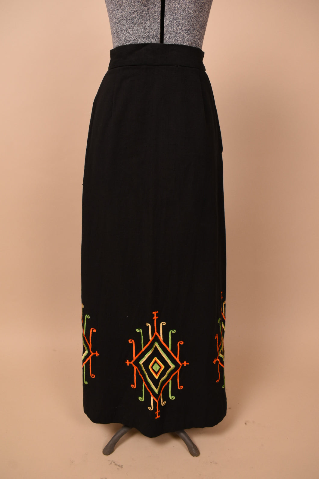 Vintage 1960's black column maxi skirt is shown from the front. This skirt has a red, green, and yellow embroidered design at the bottom hem. 