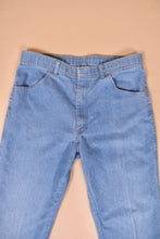 Load image into Gallery viewer, Vintage seventies light wash blue denim jeans are shown in close up. These jeans have brown stitching. 

