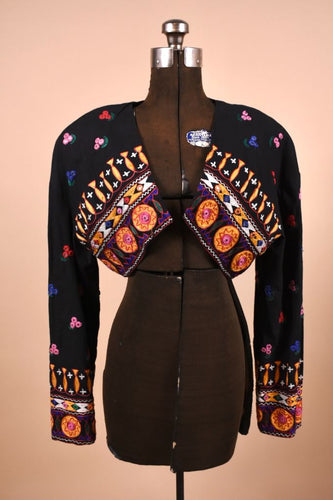 Vintage black Anna Sui embroidered bolero jacket is shown from the front. This jacket has a brightly colored abstract embroidered design with mirrored accents. 