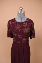 Load image into Gallery viewer, Vintage 1990s burgundy short sleeve long dress is shown from the front. This dress has a gold floral pattern on the bust.
